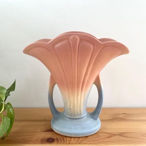 May include: A pink and blue ceramic vase with a flower-shaped design. The vase has a wide opening and two handles.