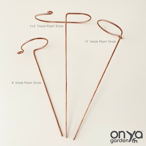 May include: Three copper plant sticks with hooks. The sticks are 9 inches, 11 inches, and 11.5 inches long. The sticks are on a white background.