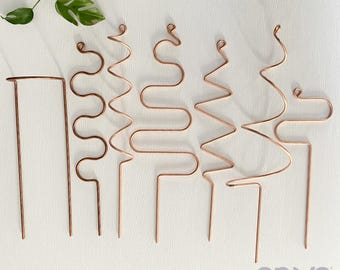 May include: A set of six copper-colored metal plant trellises with various geometric wire shapes, including spirals, zigzags, and arches, arranged in a row. The text "on ya garden" is printed in the bottom right corner of the image.