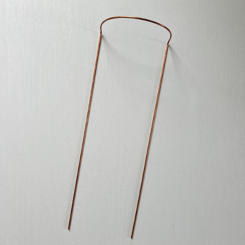 May include: A copper wire plant support with a rounded top and two straight legs.