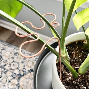 May include: A set of three copper plant supports in a wavy design. The supports are used to help a plant grow upwards.