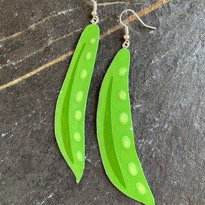 May include: A pair of green pea pod earrings with silver hooks. The earrings are made of paper and have a realistic design.