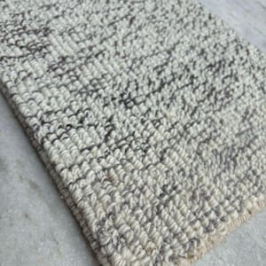 Puede incluir: Primer plano de una alfombra tejida blanca y gris con una superficie texturizada. La alfombra tiene un patrón sutil de líneas grises oscuras.