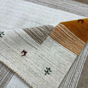 May include: A white and brown striped rug with a folded corner revealing a section of the rug with orange, brown, and white stripes. The rug has small green and red embroidered designs.