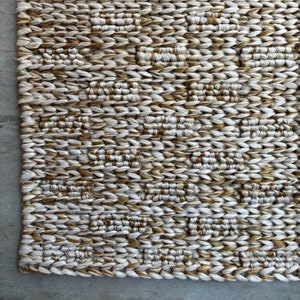 Op de afbeelding: Een geweven tapijt met een geometrisch patroon in beige en gouden tinten.