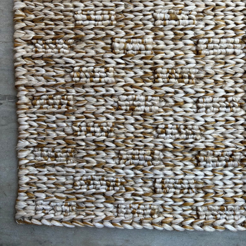 Op de afbeelding: Een geweven tapijt met een geometrisch patroon in beige en gouden tinten.