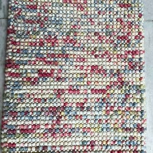 May include: A rectangular rug with a textured, beaded surface. The rug features a pattern of small, tightly packed beads in a mix of colors, including white, red, blue, and yellow. The rug is designed for indoor use.