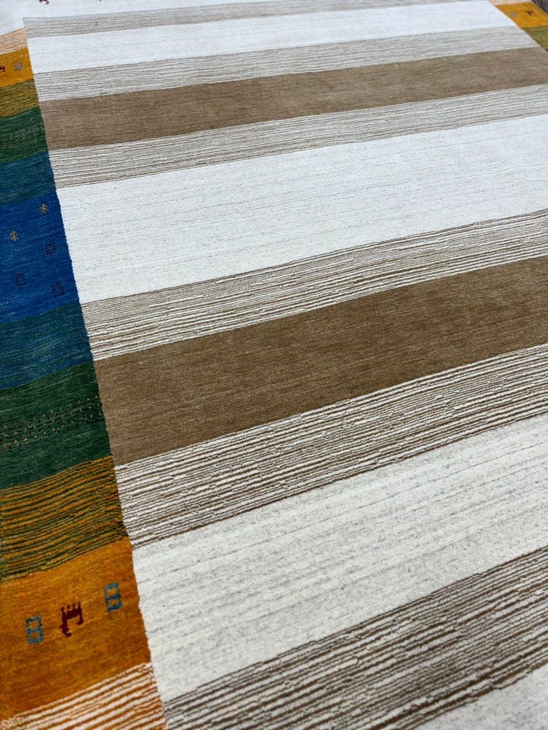 May include: A white and brown striped rug with a colorful border. The border features stripes of orange, yellow, green, blue, and red.