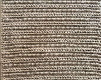 Puede incluir: Una alfombra de fibra natural con textura tejida en color marrón claro.