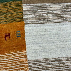May include: A close-up of a woven rug with a geometric pattern. The rug is made of different colored yarns, including green, yellow, orange, and white. The rug has a textured surface.