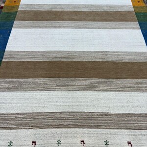 May include: A white and brown striped rug with a subtle texture. The rug has a border with small green trees and red castle-like designs.