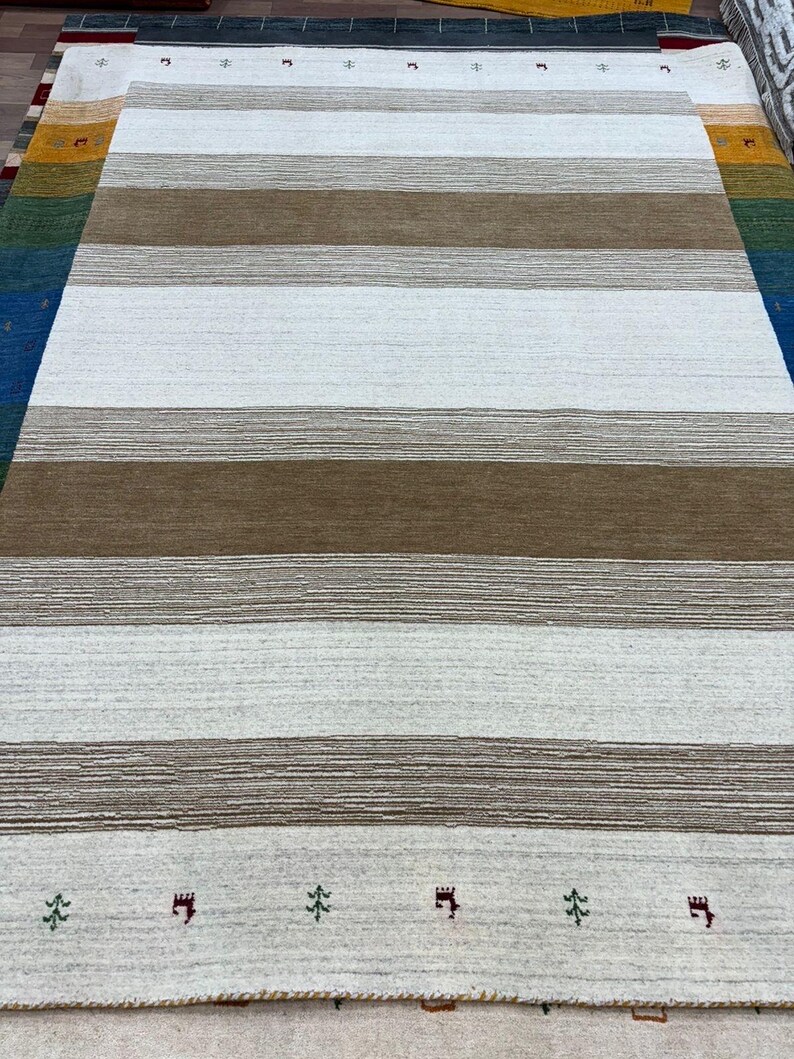 May include: A white and brown striped rug with a subtle texture. The rug has a border with small green trees and red castle-like designs.