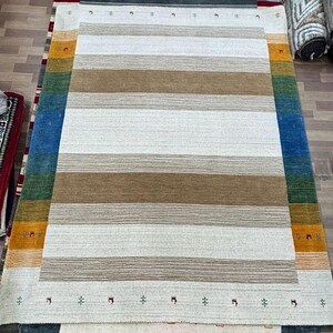 May include: A white and brown striped rug with a border of blue, green, orange, and yellow. The rug has a subtle pattern of small symbols along the border.