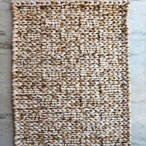 Op de afbeelding: Een geweven tapijt met een beige en bruin patroon. Het tapijt is gemaakt van natuurlijke vezels en heeft een textuur.