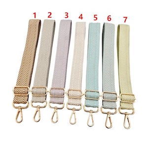 May include: Seven colorful bag straps with gold-colored metal clasps and swivel hooks. The straps are in shades of beige, gray, lavender, off-white, light blue, gray-green, and pale yellow. Each strap has a chevron pattern.