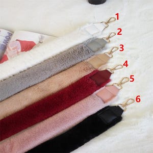 May include: Six different faux fur handbag straps with gold hardware. The straps are in various colors, including white, gray, pink, red, and black.