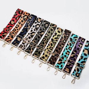 Könnte beinhalten: Ein Set aus zehn bunten, verstellbaren Riemen mit Leopardenmuster und goldfarbener Metallbeschläge. Die Riemen sind aus gewebtem Stoff und haben eine Vielzahl von Farben, darunter Rot, Orange, Gelb, Grün, Blau, Lila und Schwarz.
