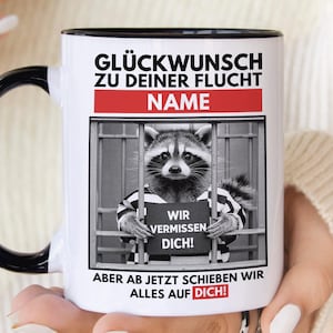 Könnte beinhalten: Weiße Keramiktasse mit schwarzem Henkel und schwarzem Rand. Die Tasse zeigt ein Schwarzweißbild eines Waschbären, der eine gestreifte Gefängnisuniform trägt und ein Schild mit der Aufschrift "Wir vermissen dich!" (Wir vermissen dich!) hält. Der Text auf der Tasse lautet "Glückwunsch zu deiner Flucht NAME ABER AB JETZT SCHIEBEN WIR ALLES AUF DICH!" (Glückwunsch zu deiner Flucht NAME aber jetzt schieben wir alles auf dich!).