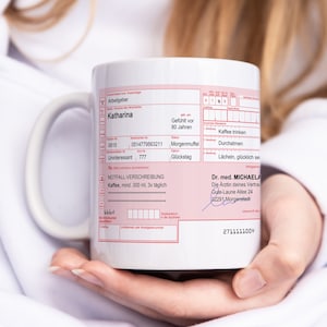 K&ouml;nnte beinhalten: Wei&szlig;e Keramiktasse mit einem roten und wei&szlig;en medizinischen Rezeptformular darauf gedruckt. Das Formular enth&auml;lt den Text "NOTFALL-VERSCHREIBUNG" und "Kaffee, mind. 300 ml, 3x t&auml;glich". Das Formular enth&auml;lt auch den Text "Dr. med. MICHAELA" und "Die &Auml;rztin deines Vertrau".