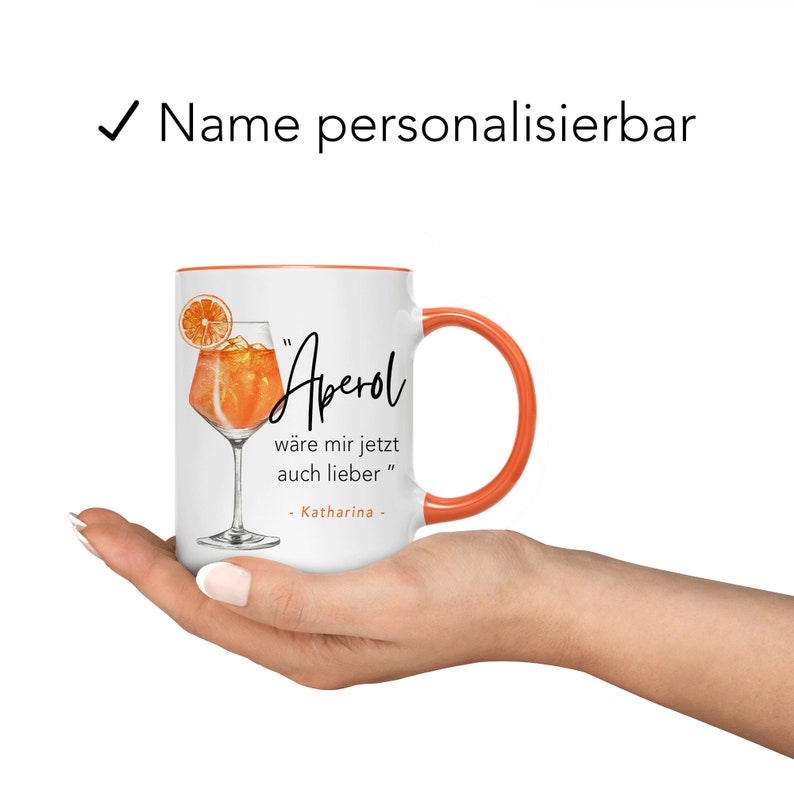 K&ouml;nnte beinhalten: Wei&szlig;e Keramiktasse mit orangefarbenem Rand und Henkel. Die Tasse zeigt eine Grafik eines Aperol Spritz Cocktails und den Text "Aperol" in schwarzer Schrift. Der Text unter der Grafik lautet "w&auml;re mir jetzt auch lieber" und "Katharina".