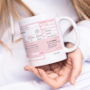 K&ouml;nnte beinhalten: Wei&szlig;e Keramiktasse mit einem rosafarbenen Design im Stil eines Rezepts. Die Tasse zeigt den Text "Deine beste Freundin Martina" und "Dr. med. HANNAH Die Arztin deines Vertrauens Gule-Laune Allee 24 2291 Morganstadt".