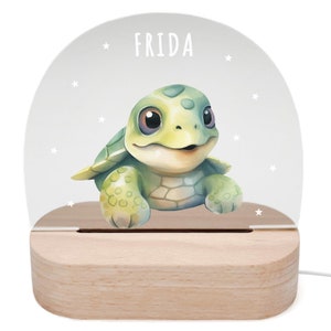 May include: A night light with a wooden base and a clear acrylic dome featuring a cartoon turtle with a green shell and a name "FRIDA" printed on the dome.