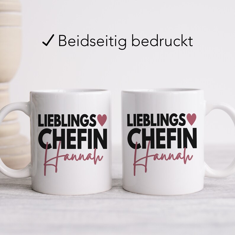 May include: Two white ceramic mugs with black text that reads "Lieblings Chefin Hannah" and a pink heart. The mugs are printed on both sides.