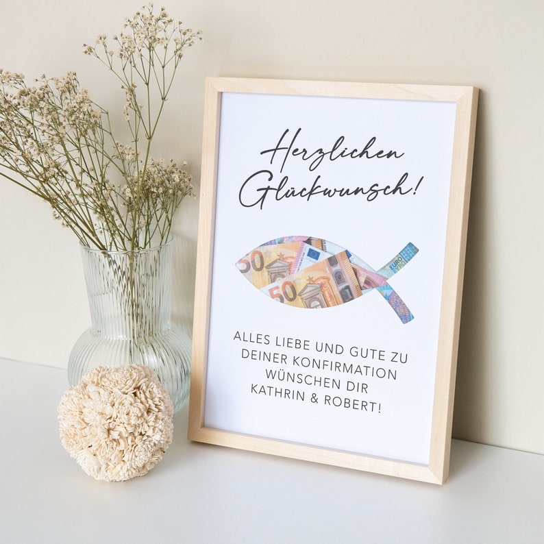 May include: A white framed picture with a fish-shaped cutout filled with euro bills. The text reads "Herzlichen Gl&uuml;ckwunsch!" and "ALLES LIEBE UND GUTE ZU DEINER KONFIRMATION W&Uuml;NSCHEN DIR KATHRIN & ROBERT!"