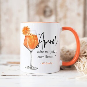 K&ouml;nnte beinhalten: Wei&szlig;e Keramiktasse mit orangefarbenem Rand und Henkel. Die Tasse zeigt eine Grafik eines Aperol Spritz Cocktails und den Text "Aperol w&auml;re mir jetzt auch lieber" - Michaela.