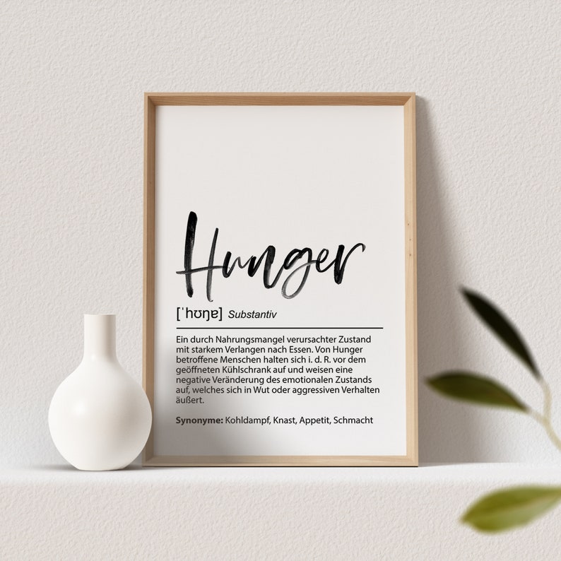 May include: A framed print with the word "Hunger" in a handwritten style. The print includes a definition in German, a white vase, and a sprig of greenery.