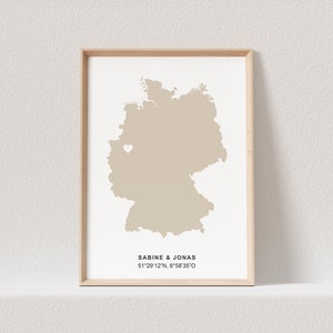 Könnte beinhalten: Eine beigefarbene Karte von Deutschland mit einem weißen Herzen, das einen Ort markiert. Der Text darunter lautet "Sabine & Jonas 51°29'12"N, 6°58'35"O".