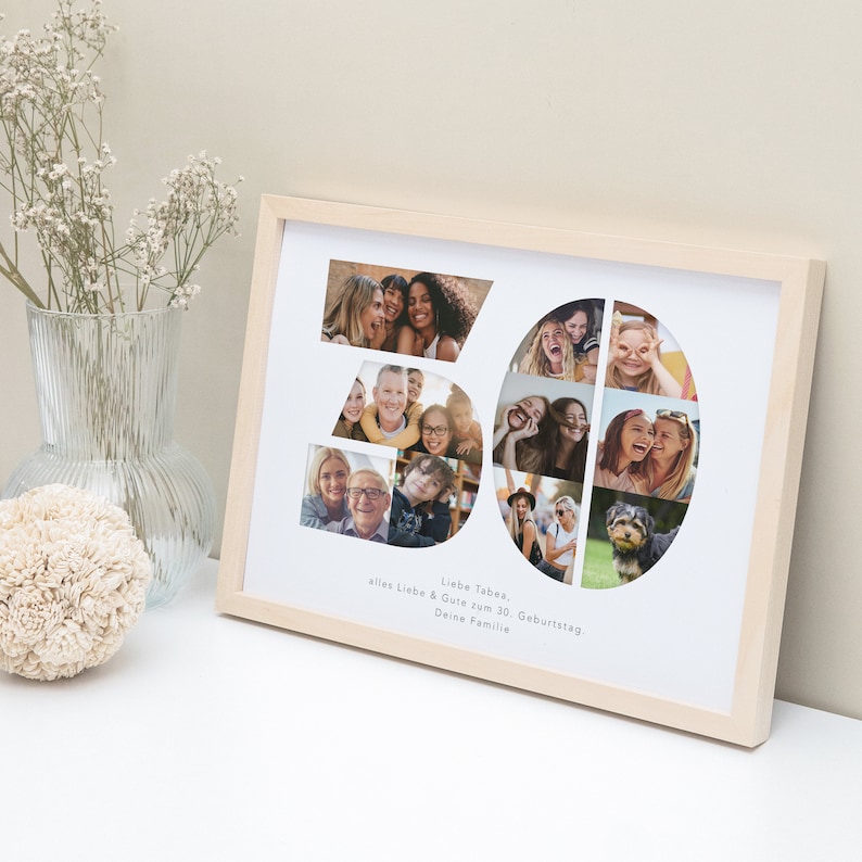 May include: A white photo frame with a light wood frame. The frame contains a collage of photos arranged in the shape of the number 30. The text "Liebe Tabea, alles Liebe & Gute zum 30. Geburtstag, Deine Familie" is printed below the collage.