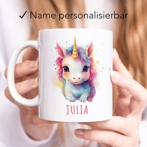 May include: White ceramic mug featuring a colourful watercolour illustration of a unicorn with a gold horn. The name "JULIA" is printed in pink below the unicorn.
