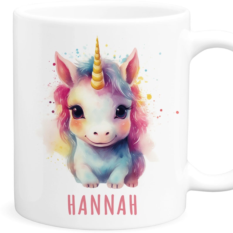 May include: White ceramic mug featuring a colourful watercolour illustration of a unicorn with a gold horn. The unicorn has pink, blue and yellow accents. The name "HANNAH" is printed in pink below the unicorn.