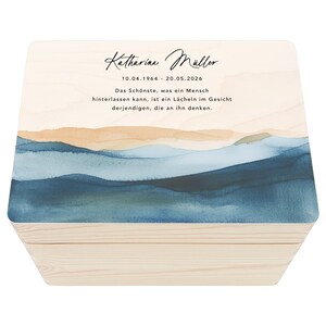 Könnte beinhalten: Eine Holzkiste mit einer hellen Holzoptik und einem blauen und orangenen Aquarelldesign auf dem Deckel. Der Deckel trägt den Text "Katharina Müller 10.04.1964 - 20.05.2026" und ein Zitat darüber, ein Lächeln zurückzulassen.