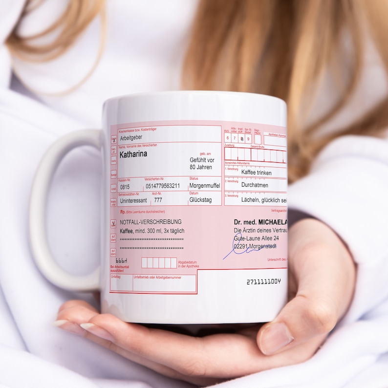 K&ouml;nnte beinhalten: Wei&szlig;e Keramiktasse mit einem roten und wei&szlig;en medizinischen Rezeptformular darauf gedruckt. Das Formular enth&auml;lt den Text "NOTFALL-VERSCHREIBUNG" und "Kaffee, mind. 300 ml, 3x t&auml;glich". Das Formular enth&auml;lt auch den Text "Dr. med. MICHAELA" und "Die &Auml;rztin deines Vertrau".