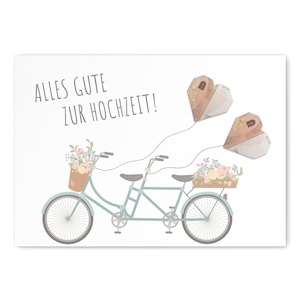 Puede incluir: Una bicicleta tándem azul claro con una cesta de flores en la parte delantera. Dos cometas en forma de corazón blanco con la palabra "Forever" escrita en ellos están volando en el cielo. El texto "Alles Gute zur Hochzeit!" está escrito en la tarjeta.