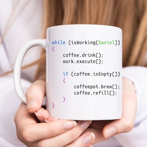 Könnte beinhalten: Eine weiße Keramiktasse mit einem humorvollen Programmiercode darauf gedruckt. Der Code lautet: "while (isWorking(Daniel)) { coffee.drink(); work.execute(); if (coffee.isEmpty()) { coffeepot.brew(); coffee.refill(); } }"
