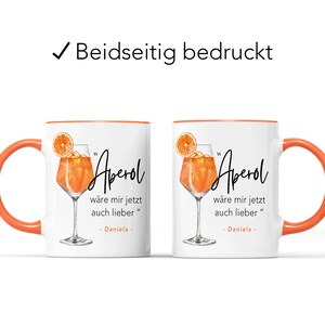 K&ouml;nnte beinhalten: Wei&szlig;e Keramiktasse mit orangefarbenem Rand. Die Tasse zeigt eine Grafik eines Aperol Spritz Cocktails mit dem Text "Aperol" und dem Satz "w&auml;re mir jetzt auch lieber" in Schwarz. Der Text "Daniela" ist ebenfalls in Schwarz enthalten.