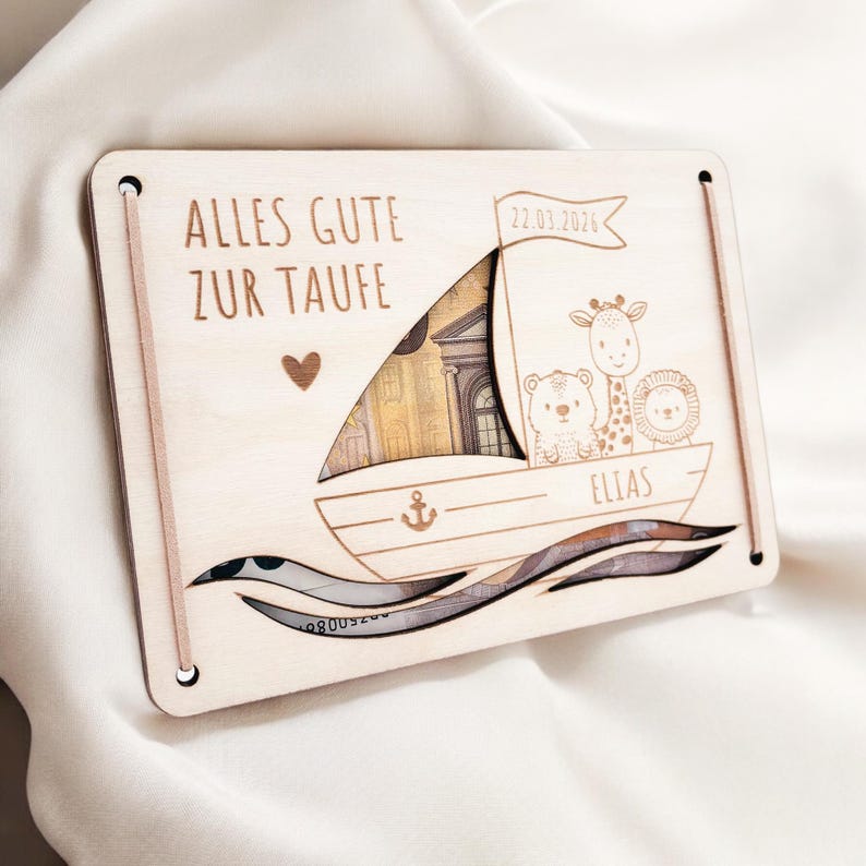 K&ouml;nnte beinhalten: Holzk&auml;rtchen mit dem Text "Alles Gute zur Taufe" und dem Datum "22.03.2026". Die Karte zeigt einen Ausschnitt eines Bootes mit Tieren darauf, darunter eine Giraffe, ein B&auml;r und ein L&ouml;we. Der Name "Elias" steht auf dem Boot.