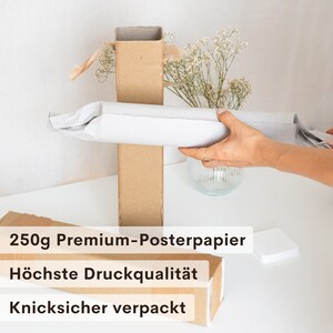 May include: A rolled poster is being carefully placed into a cardboard tube. The tube is wrapped in brown paper and secured with tape. The poster is protected by a white paper wrapping. The text on the box reads "250g Premium-Posterpapier", "H&ouml;chste Druckqualit&auml;t", and "Knicksicher verpackt".