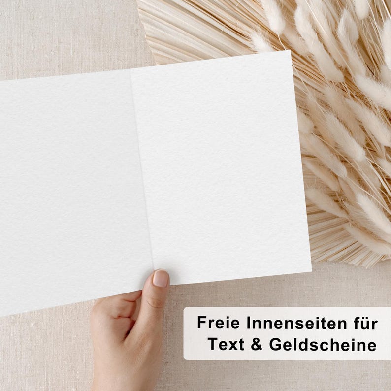 May include: A blank white card with a textured surface. The card is folded in half and is being held by a hand. The text "Freie Innenseiten f&uuml;r Text & Geldgeschenke" is visible at the bottom of the image.