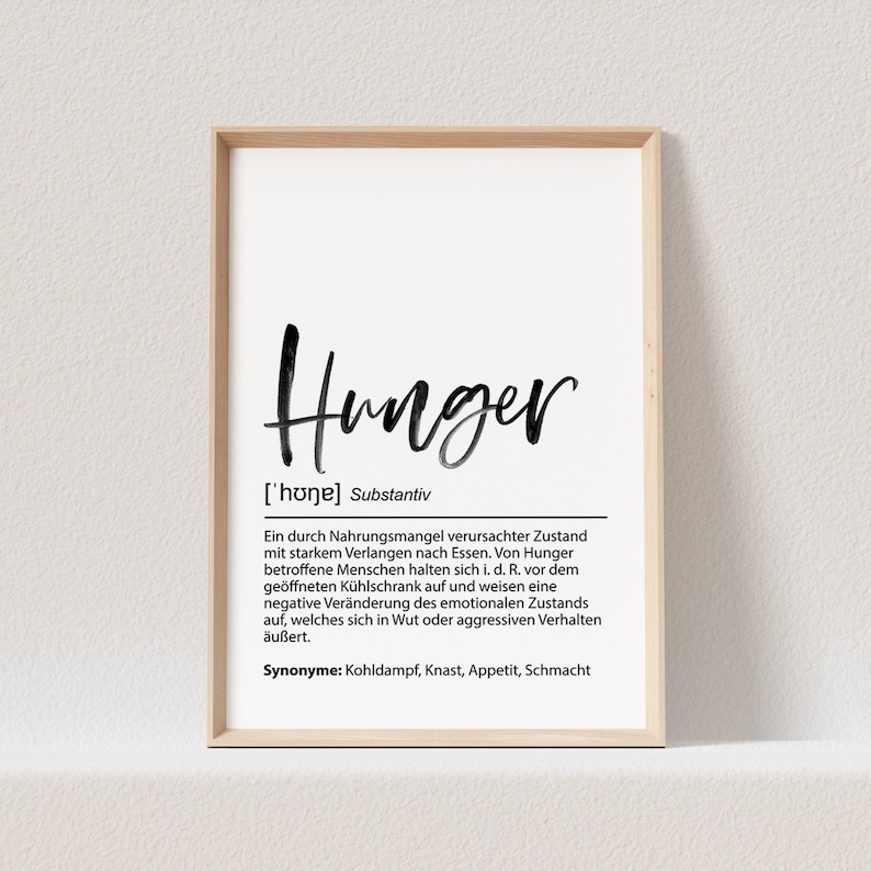 May include: A framed print with the word "Hunger" in a black, handwritten font. Below the word is a definition in German, with the phonetic pronunciation and synonyms listed. The frame is a light wood color.