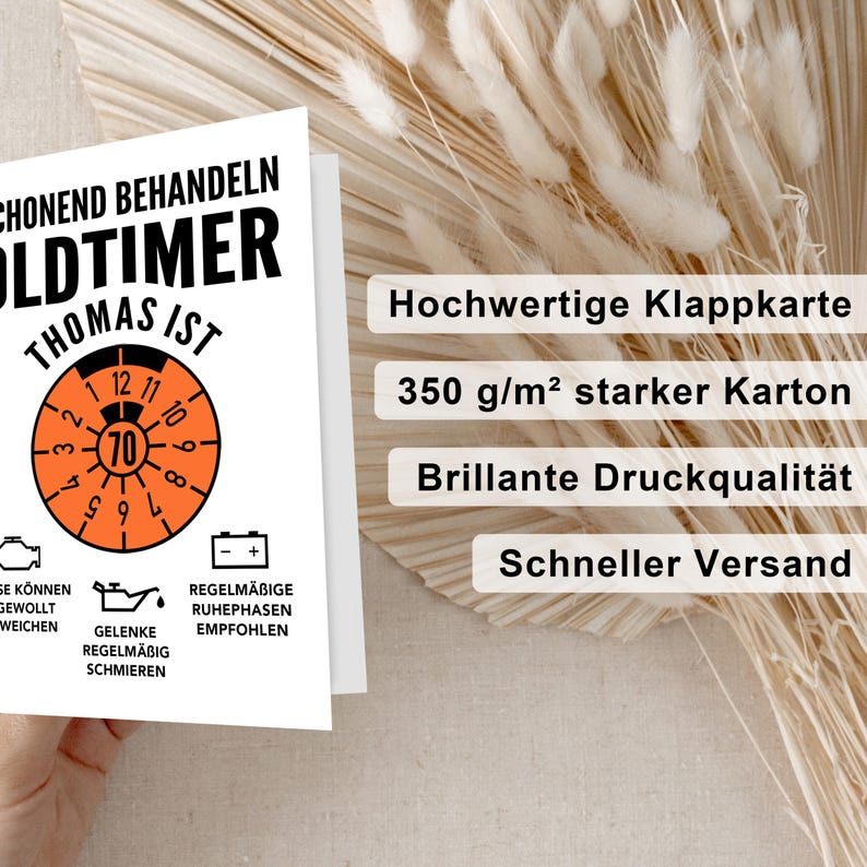 May include: A white card with black and orange text and a black and orange speedometer graphic. The text reads "CHONEND BEHANDELN OLDTIMER THOMAS IST". The speedometer graphic has a black needle pointing to the number 70. The card also has a black and orange illustration of a car engine and a black and orange battery. The text below the speedometer graphic reads "REGELM&Auml;BIGE RUHEPHASEN EMPFOHLEN" and "GELENKE REGELM&Auml;BIG SCHMIEREN". The card is on a background of beige and white.