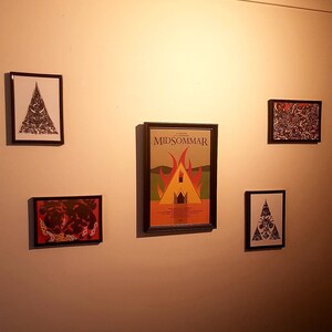 May include: A wall gallery with four framed prints. The center print is a movie poster for the film "Midsommar" with a red, orange, and yellow image of a burning building. The other three prints are black and white with abstract designs.