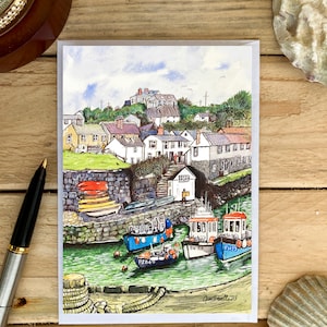 May include: A watercolour painting of a small coastal town with colourful houses and boats in a harbour. The painting is on a white card with a grey border. The artist's signature is in the bottom right corner.