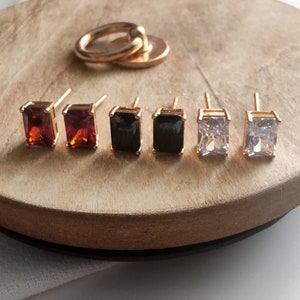 May include: Six pairs of gold earrings with different coloured gemstones. The earrings are square shaped and set with red, black and clear stones.