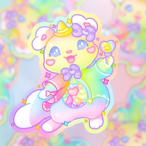 以下が含まれることがあります： 帽子をかぶって星型の杖を持ったパステルレインボーカラーの漫画のウサギ。ウサギは大きく笑っていて、ハートと星に囲まれています。
