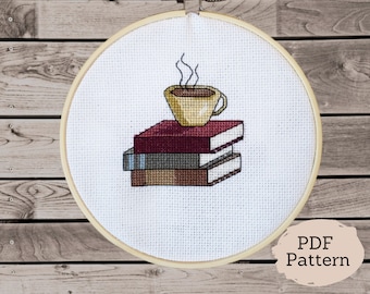 May include: A cross-stitch pattern featuring a cup of coffee on top of a stack of books. The pattern is in a white embroidery hoop on a wooden background. The text "PDF Pattern" is visible in the lower right corner of the image.