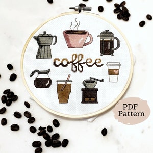Może przedstawiać: Biały tamborek do haftu z haftem krzyżykowym przedstawiającym różne metody parzenia kawy, w tym prasę francuską, dzbanek do kawy, młynek do kawy i filiżankę kawy. Tekst "coffee" jest wyszyty kursywą z wzorem ziaren kawy.